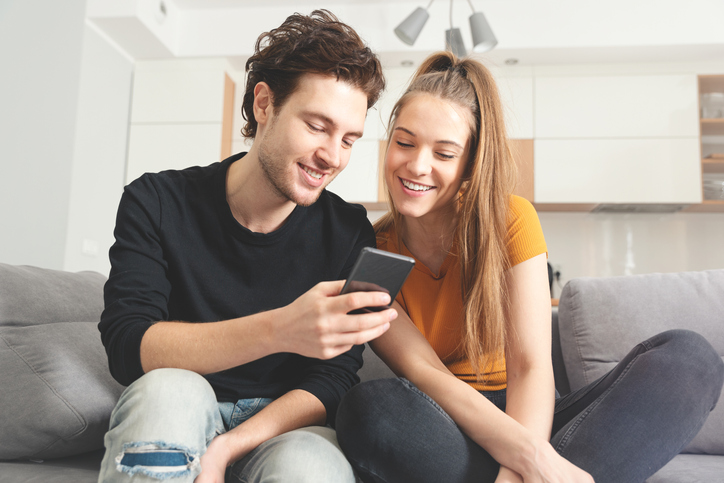 Young couple smiling and looking at a cell phone. 