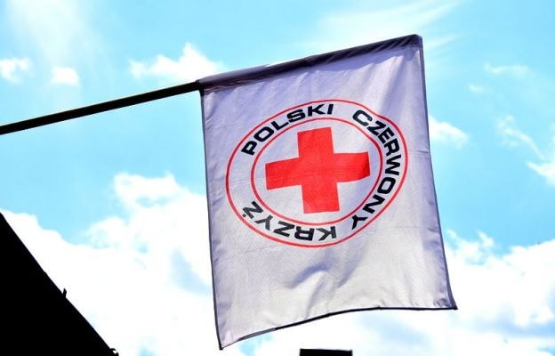 Zdjęcie białej flagi z logiem Polskiego Czerwonego Krzyża na tle niebia