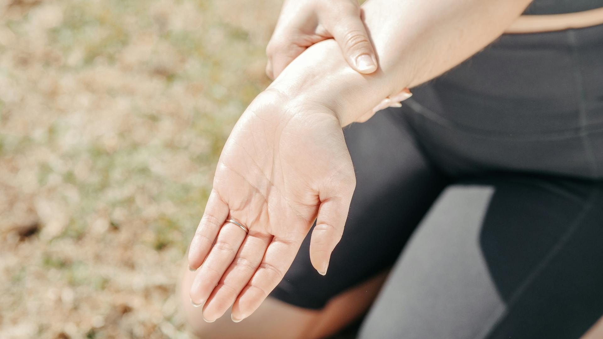 Wrist Held in Discomfort Person holding a painful wrist and hand outdoors, highlighting arthritis symptoms where finger splints may provide support.