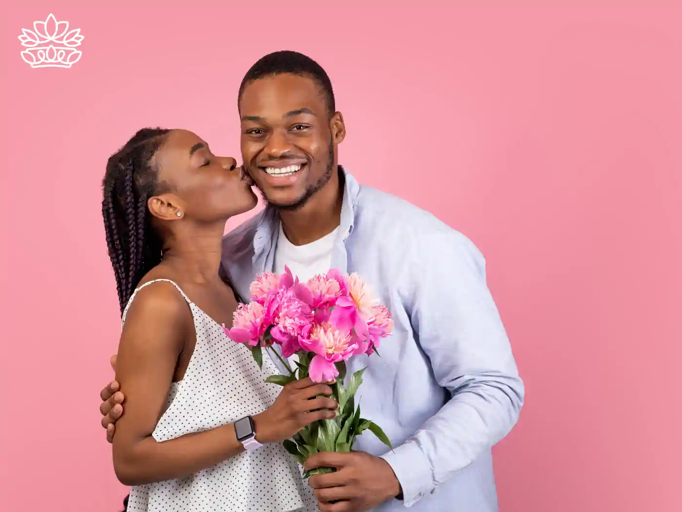 Image of a smiling woman kissing a man's cheek while he holds a pink flower bouquet against a pink background. Fabulous Flowers and Gifts - Luxury Flower Bouquets.