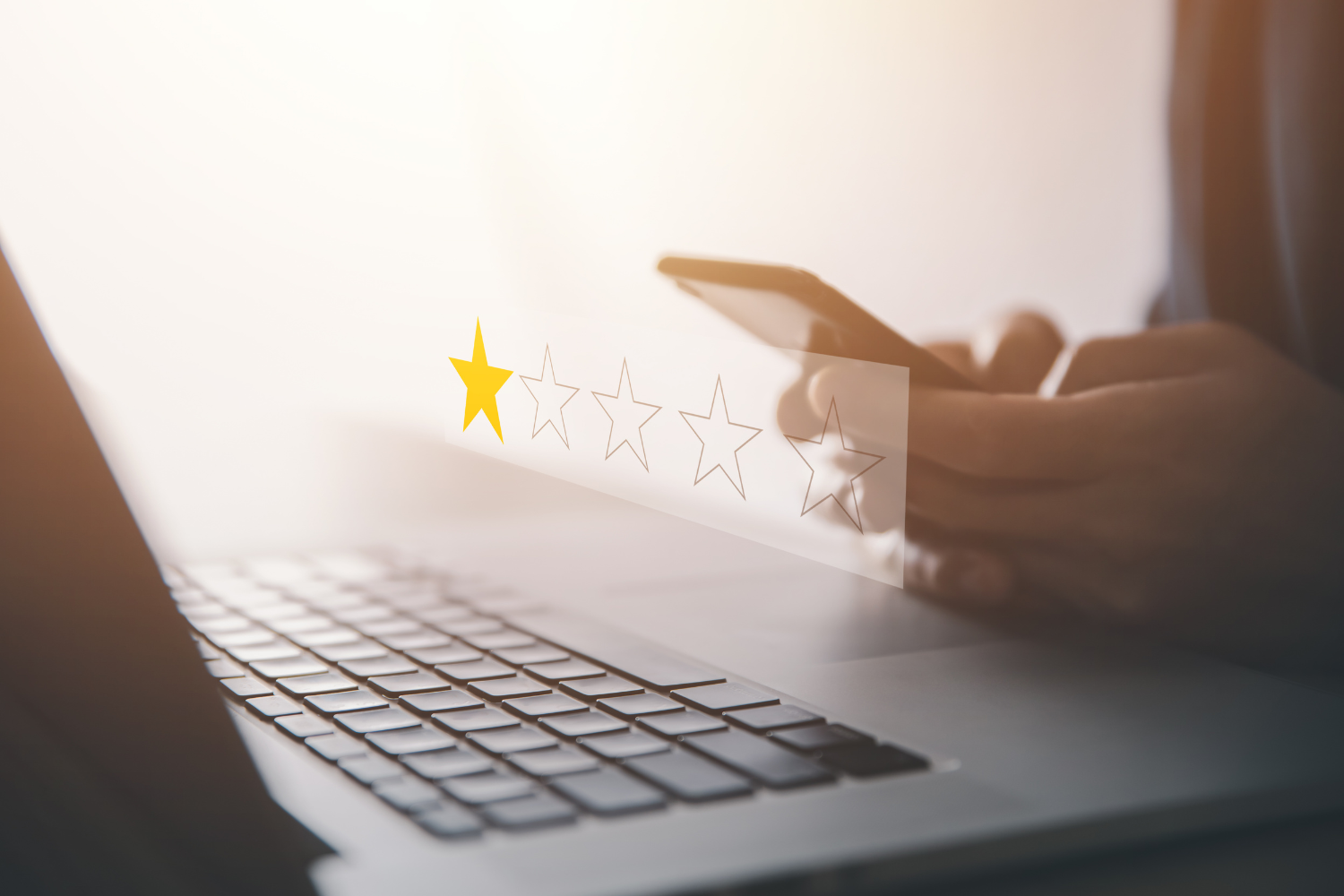 A laptop with a person using a smartphone giving one-star.