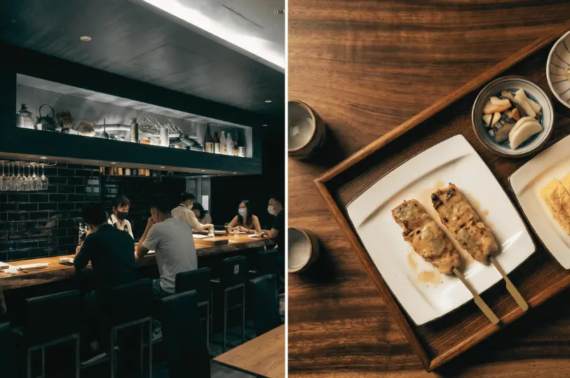 A split image showing patrons seated at a dimly lit, atmospheric izakaya counter on the left, and a wooden serving tray with two chicken yakitori skewers, pickled vegetables, and sake cups on the right.