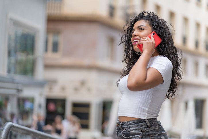 Dark-haired young woman chatting on her cell phone on a busy street.
