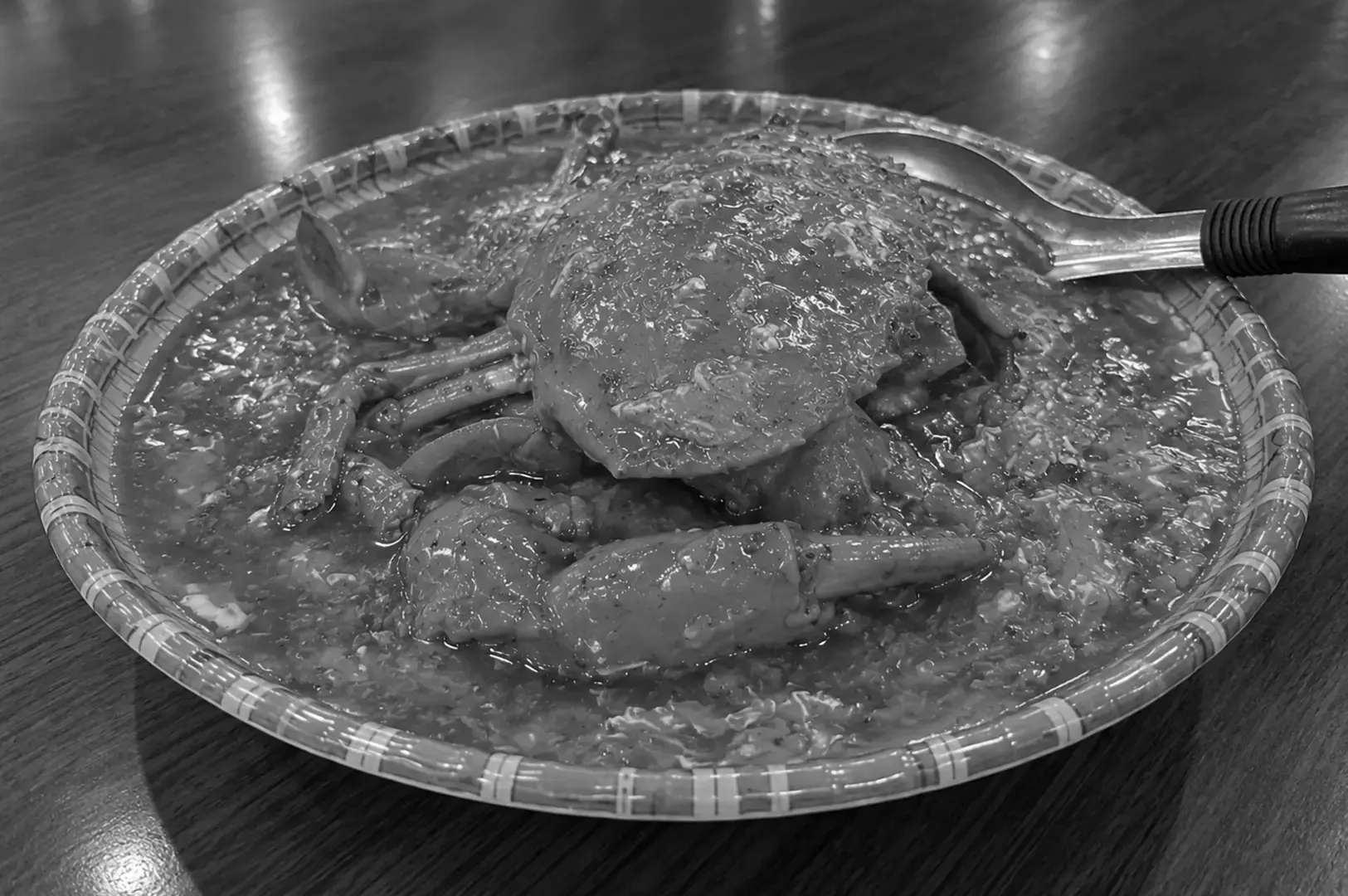 Whole chili crab served in a round patterned platter filled with rich sauce, with its shell, legs, and large claws visible alongside a metal serving spoon.