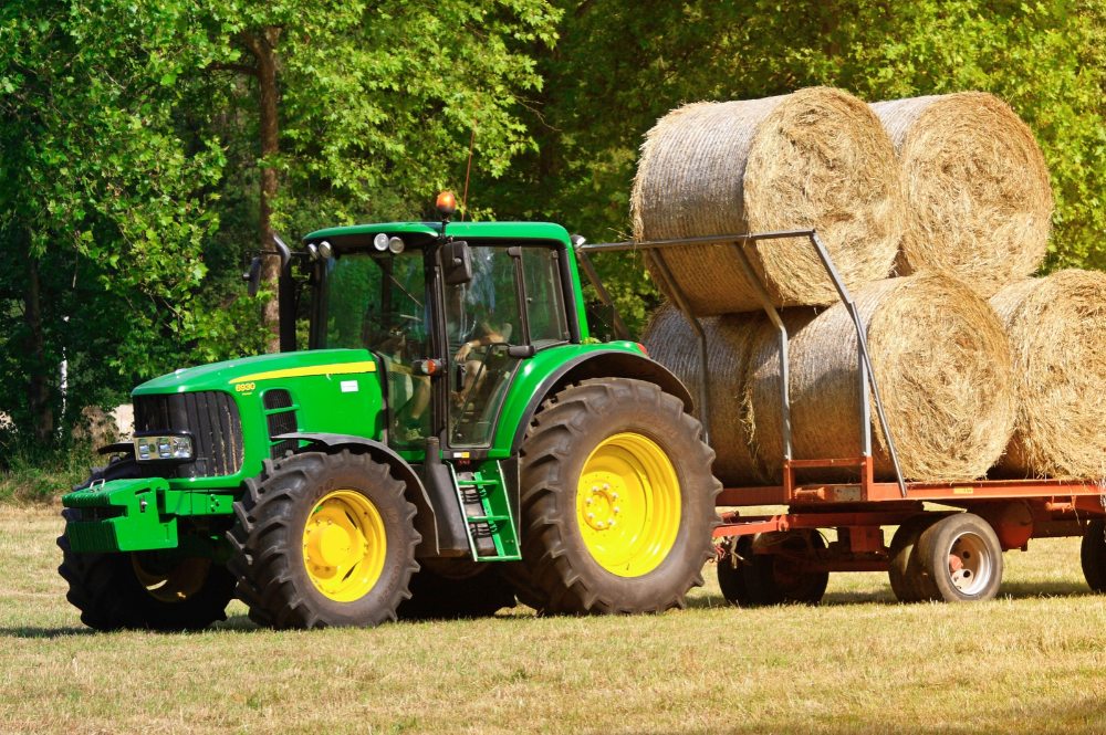 A green tractor hauling multiple bales of hay, illustrating the possibilities that a heavy equipment loan opens to farmers.