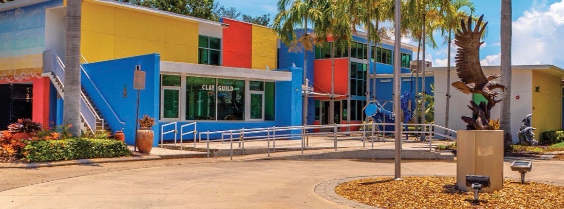 The image depicts a modern arts center building surrounded by palm trees, showcasing contemporary architecture that embodies the spirit of artistic expression. This vibrant space serves as a hub for visual and performing arts, fostering community engagement and cultural diversity in Marco Island.