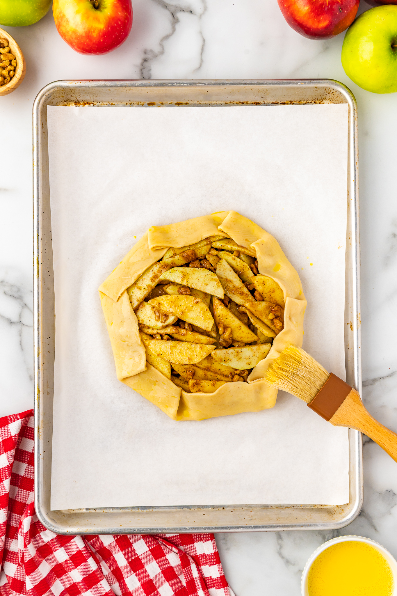 pastry brush brushing on egg wash onto unbaked apple crostata pie dough