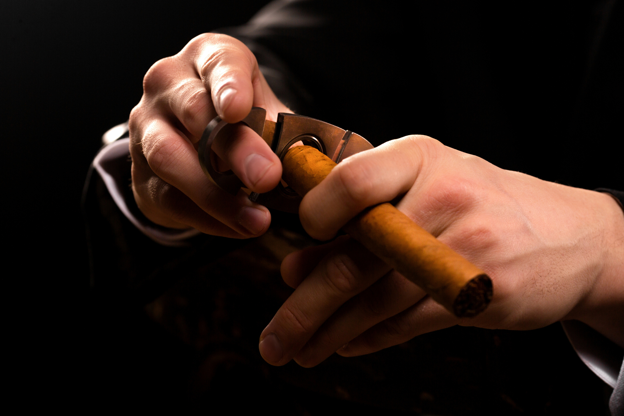 A man smoking a cigar with a premium cigar cutter in his hand
