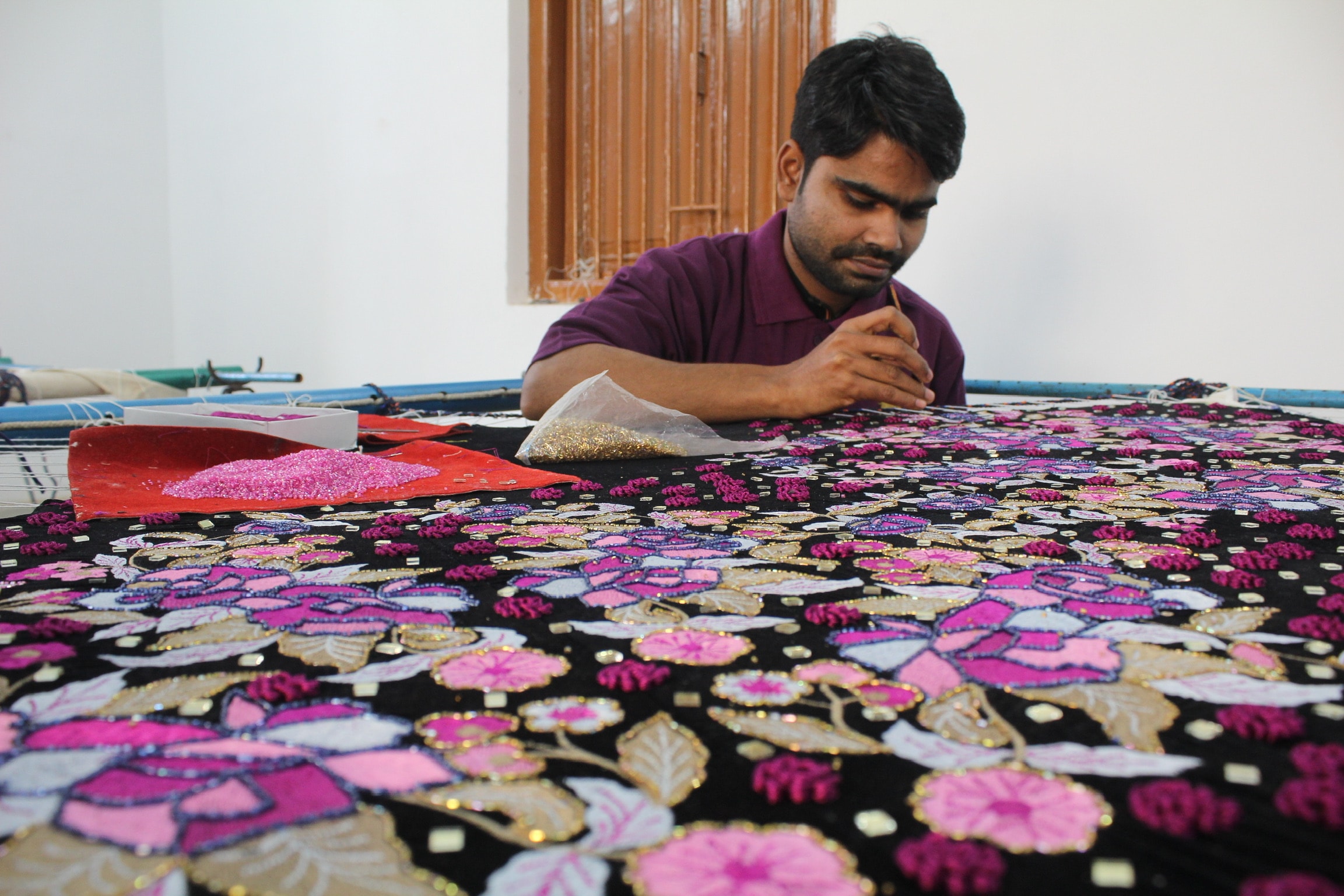 The image showcases skilled artisan meticulously crafting traditional Indian textiles and intricate embroidery work, highlighting the elegance and heritage of ethnic wear. This scene captures the essence of Indian fashion, as these artisans bring to life beautiful designs that celebrate culture and tradition.