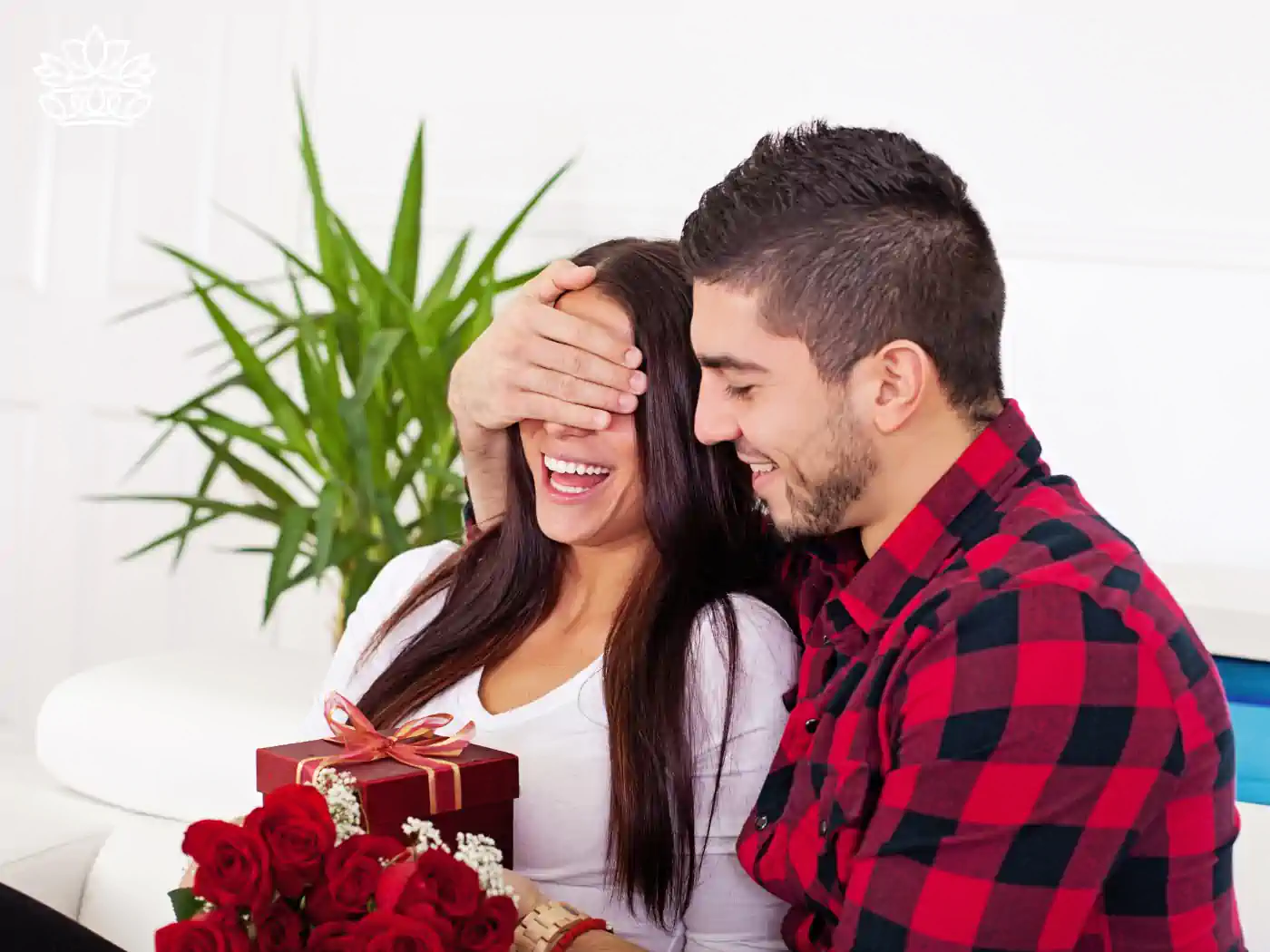 A romantic moment as a man surprises his partner with a bouquet of roses and a gift, emphasizing the joy of romantic gestures. Fabulous Flowers and Gifts.