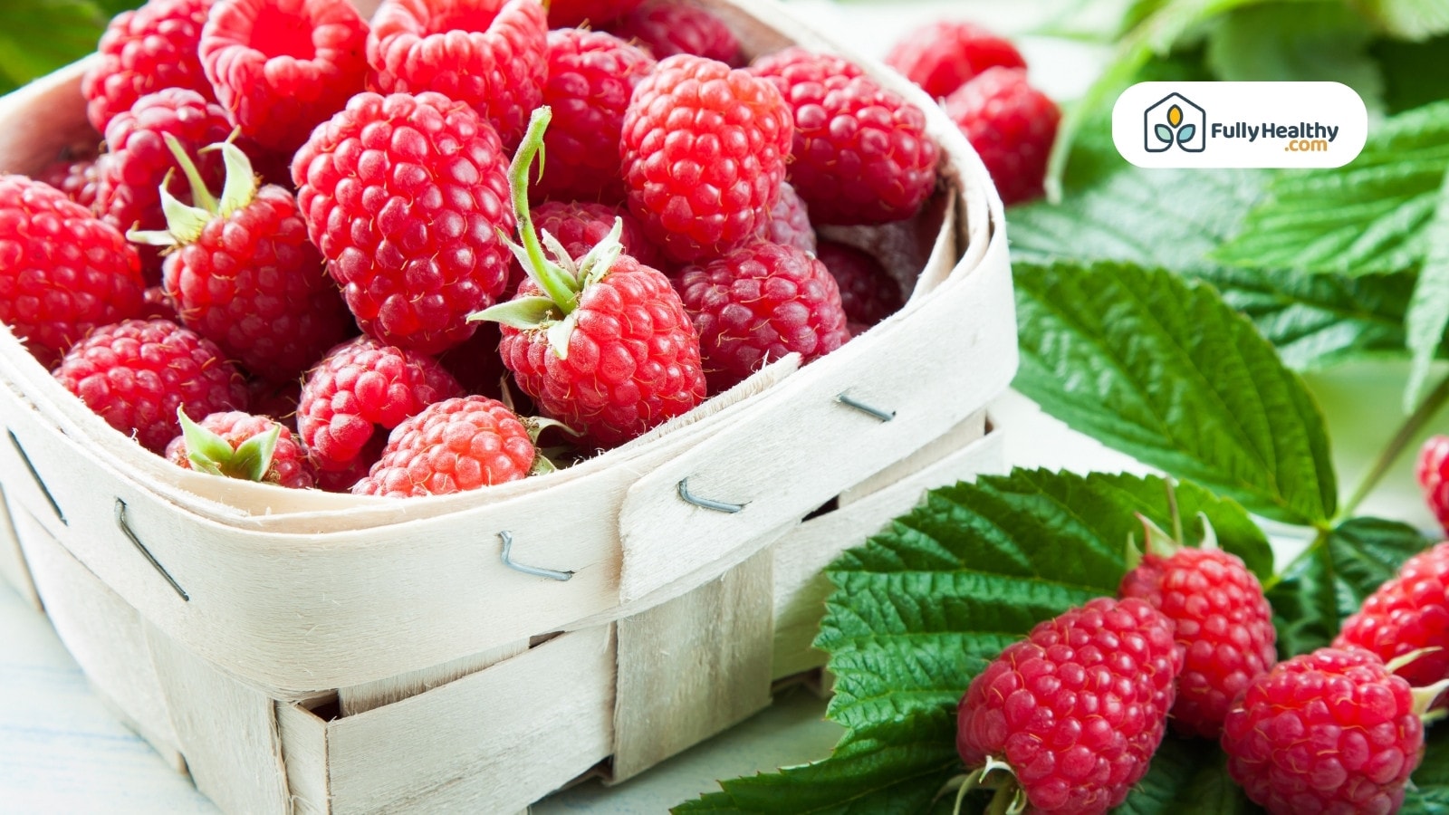 Wooden basket full of raspberries surrounded by green raspberry leaves