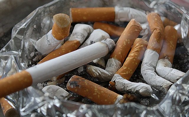 An image of an ashtray filled with cigarette butts and one lit cigarette.