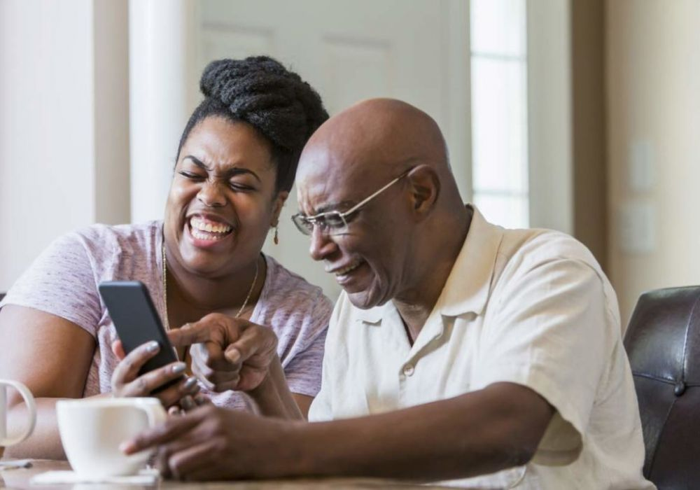 Mature couple laughing over coffee and pointing at something on a cell phone. 