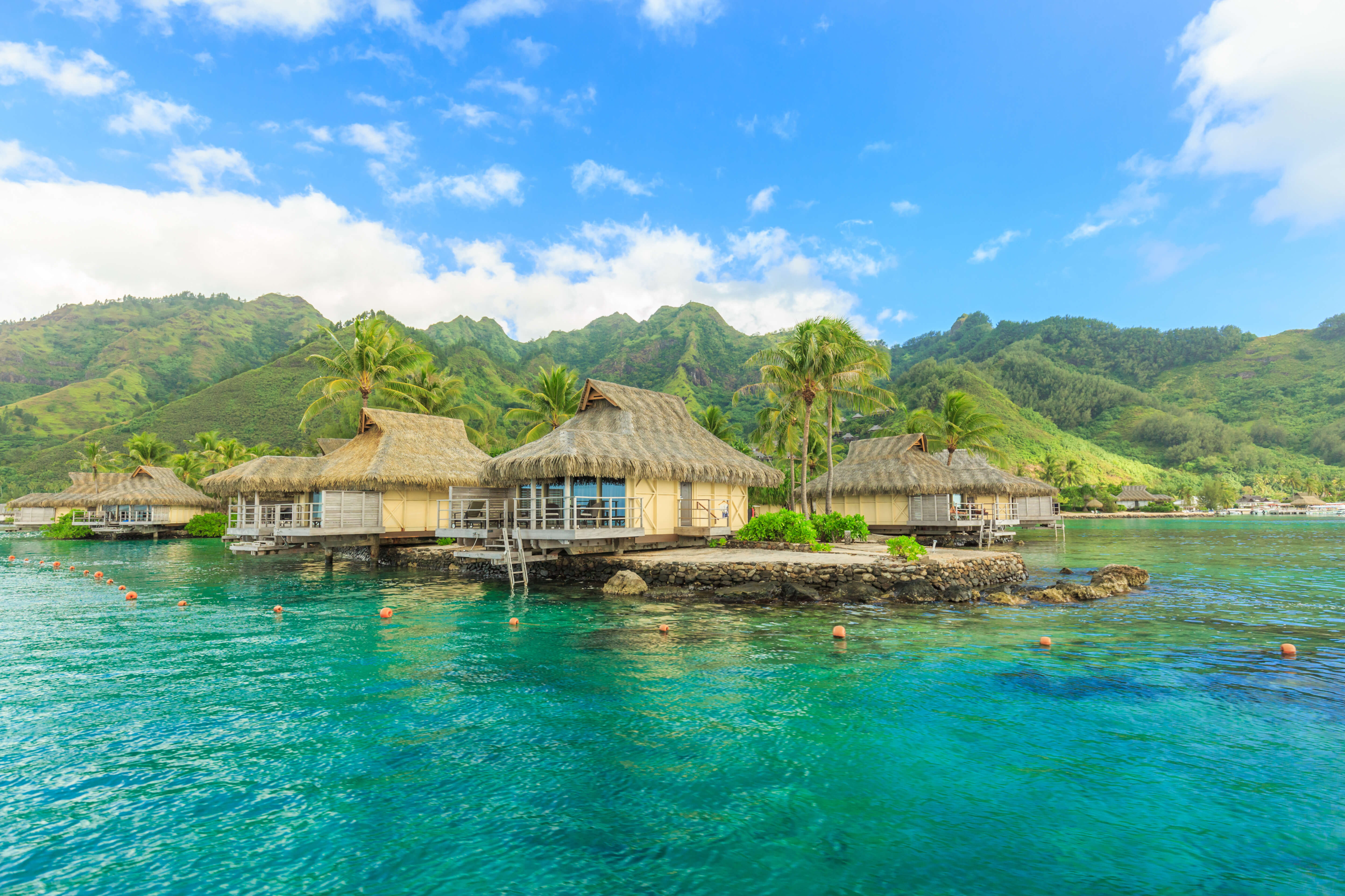 Overwater bungalows over blue ocean with a mountain in the background
    