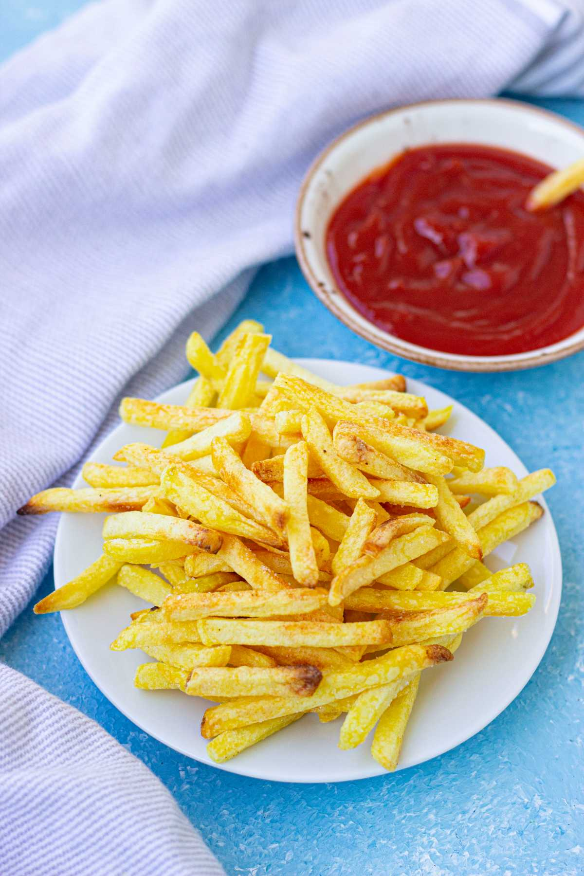Air fryer frozen french fries on a white plate with a cloth and ketchup at the side.