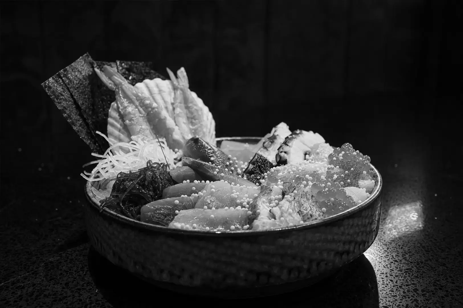 Premium chirashi don topped with assorted sashimi, ikura, tobiko, seaweed, tamagoyaki, and nori in a ceramic bowl.