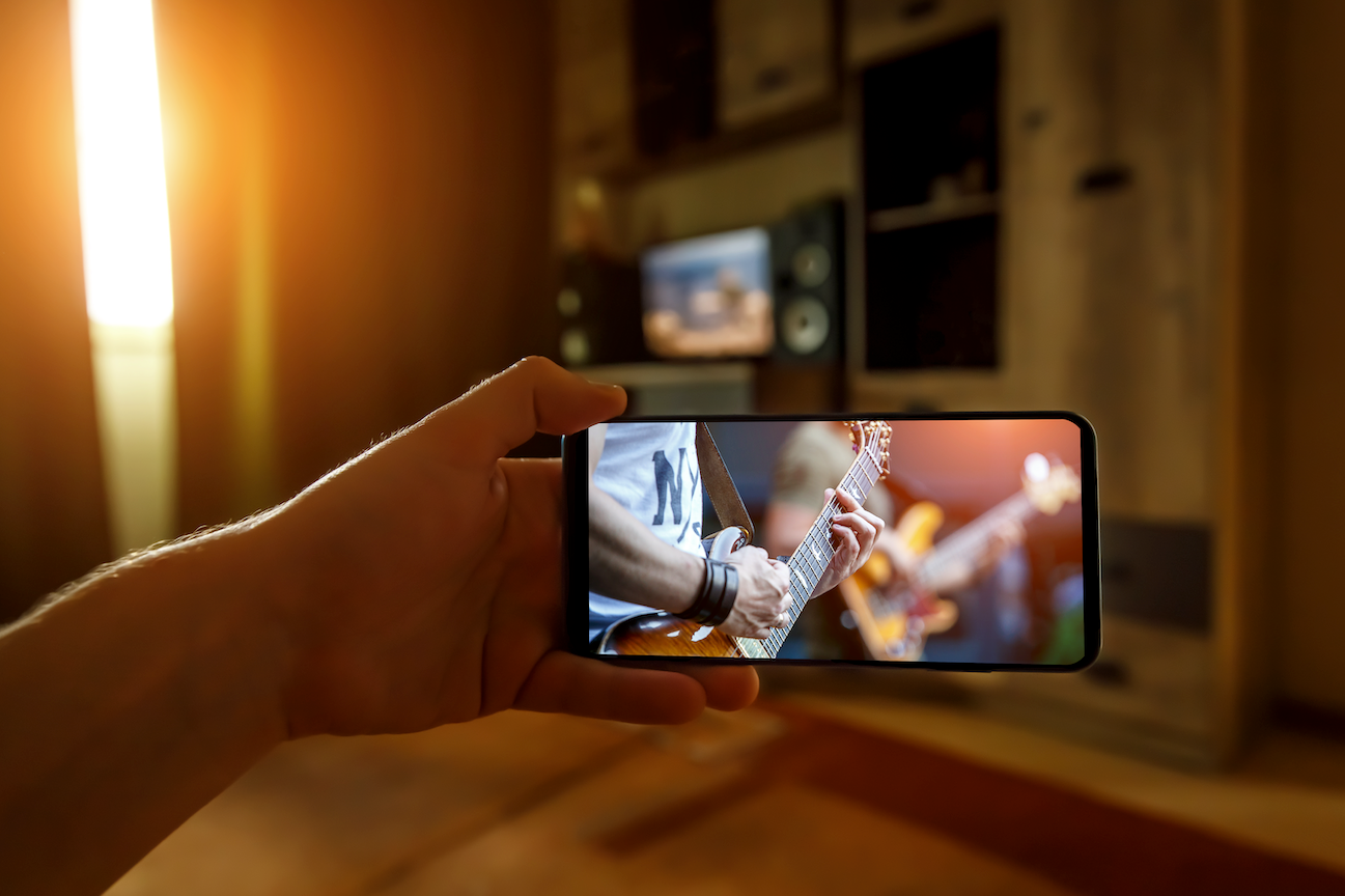 a hand holds a phone streaming the same live concert on a tv screen in the background