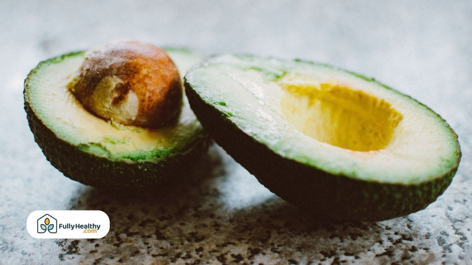 Ripe avocado halves with pit on stone background