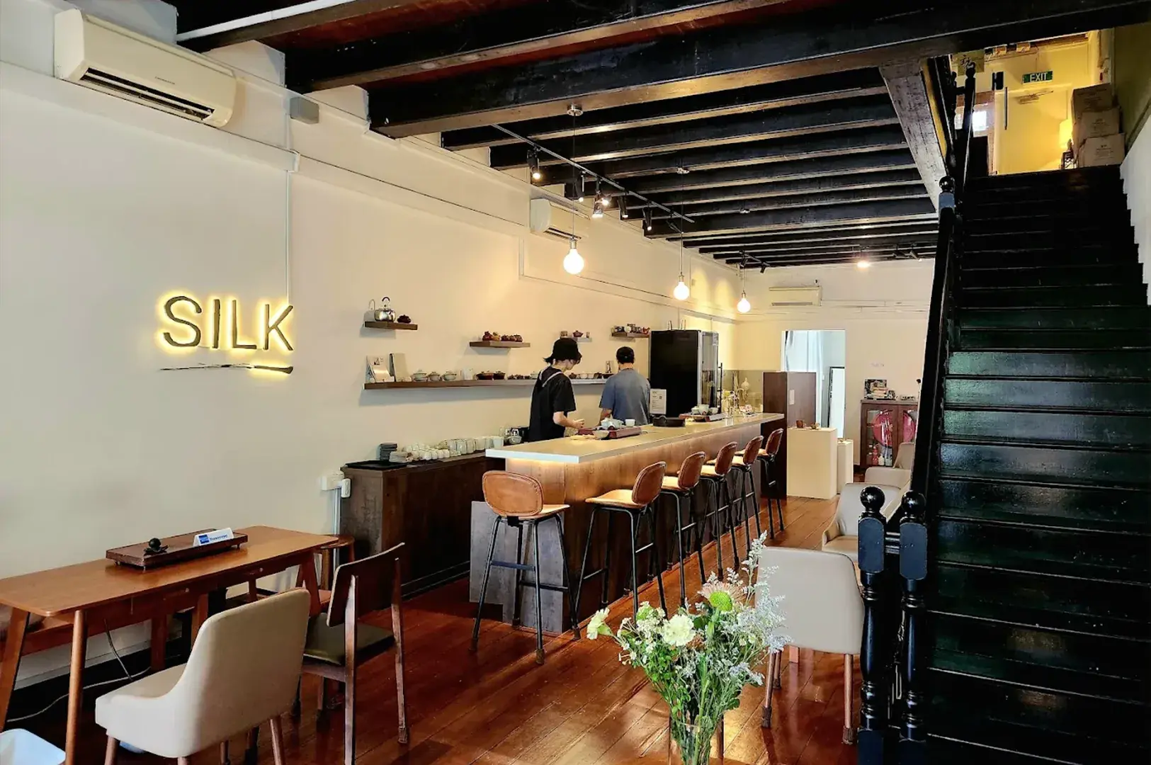 Interior of a modern tea bar with exposed ceiling beams, illuminated "SILK" sign, and counter seating.