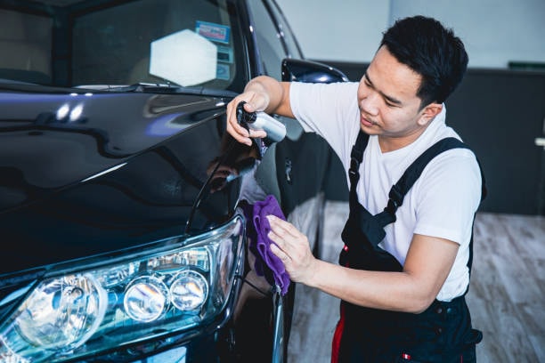 An installer skillfully wrapping Paint Protection Film (PPF) onto a car’s hood in a workshop, ensuring precision and a bubble-free application with professional tools.