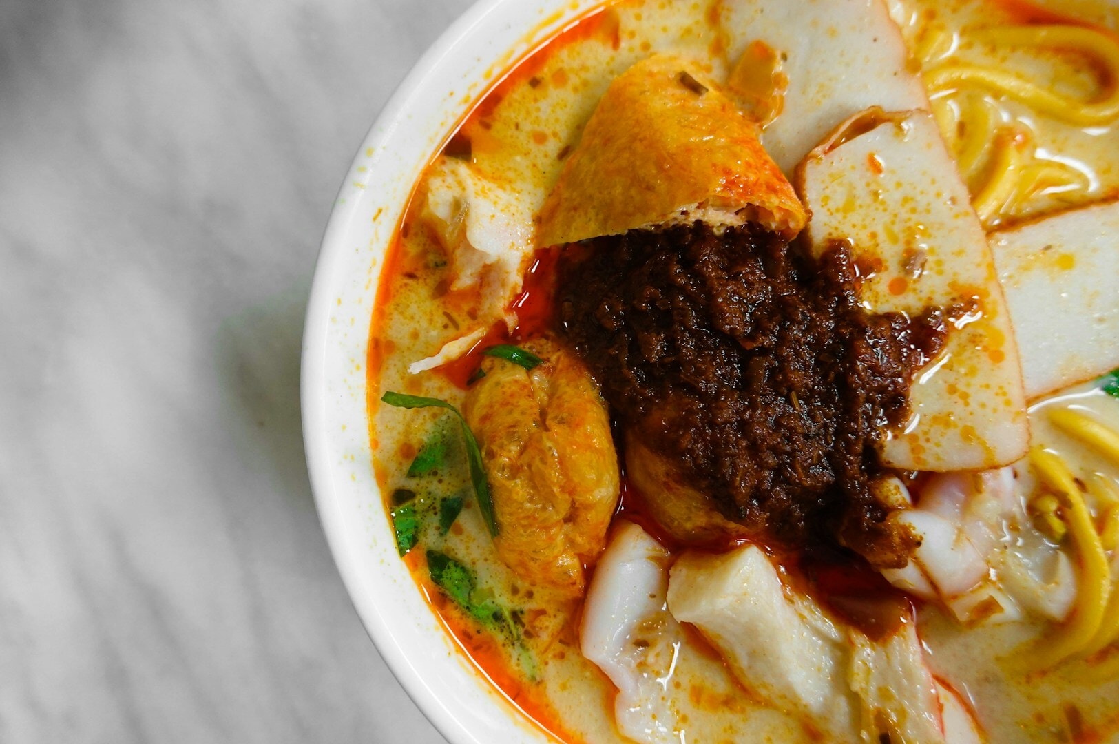 A steaming bowl of Laksa soup with noodles and meat, showcasing the rich flavors of Chinatown cuisine.