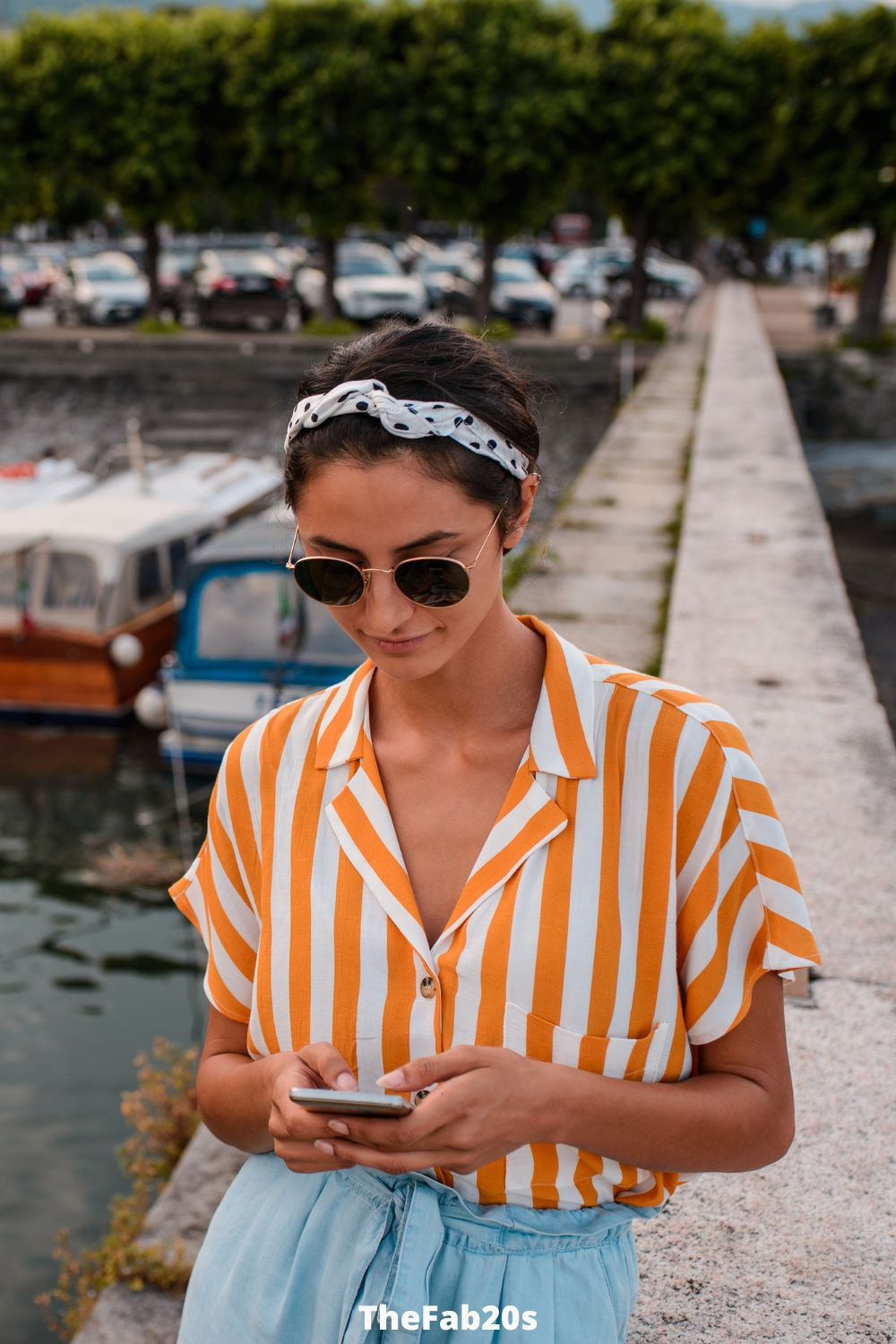 Woman in pretty yellow top textng near boats. 