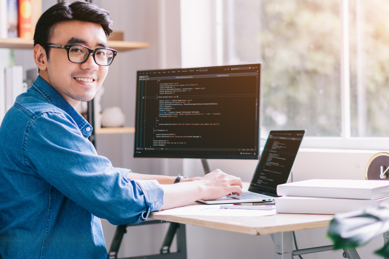 A smiling remote employee working on laptop and desktop.
