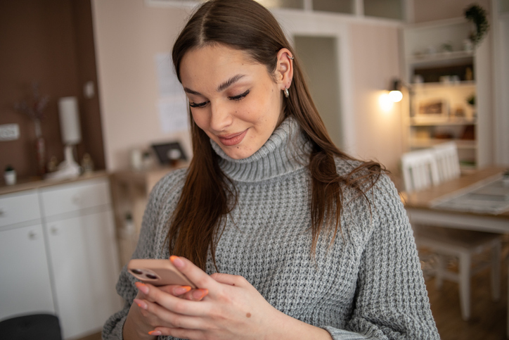 Pretty woman with long dark hair in a grey sweater sending a text. 