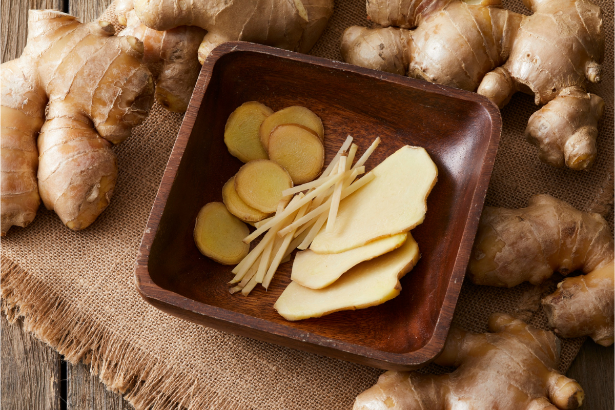 The image features a split screen comparison of fresh ginger root and ground ginger powder on a wooden cutting board, with a small pile of freshly grated ginger in the center. This educational food photography highlights the earthy flavors of ginger, an essential ingredient for fall spices used in savory dishes and baked goods, perfect for enhancing seasonal recipes.