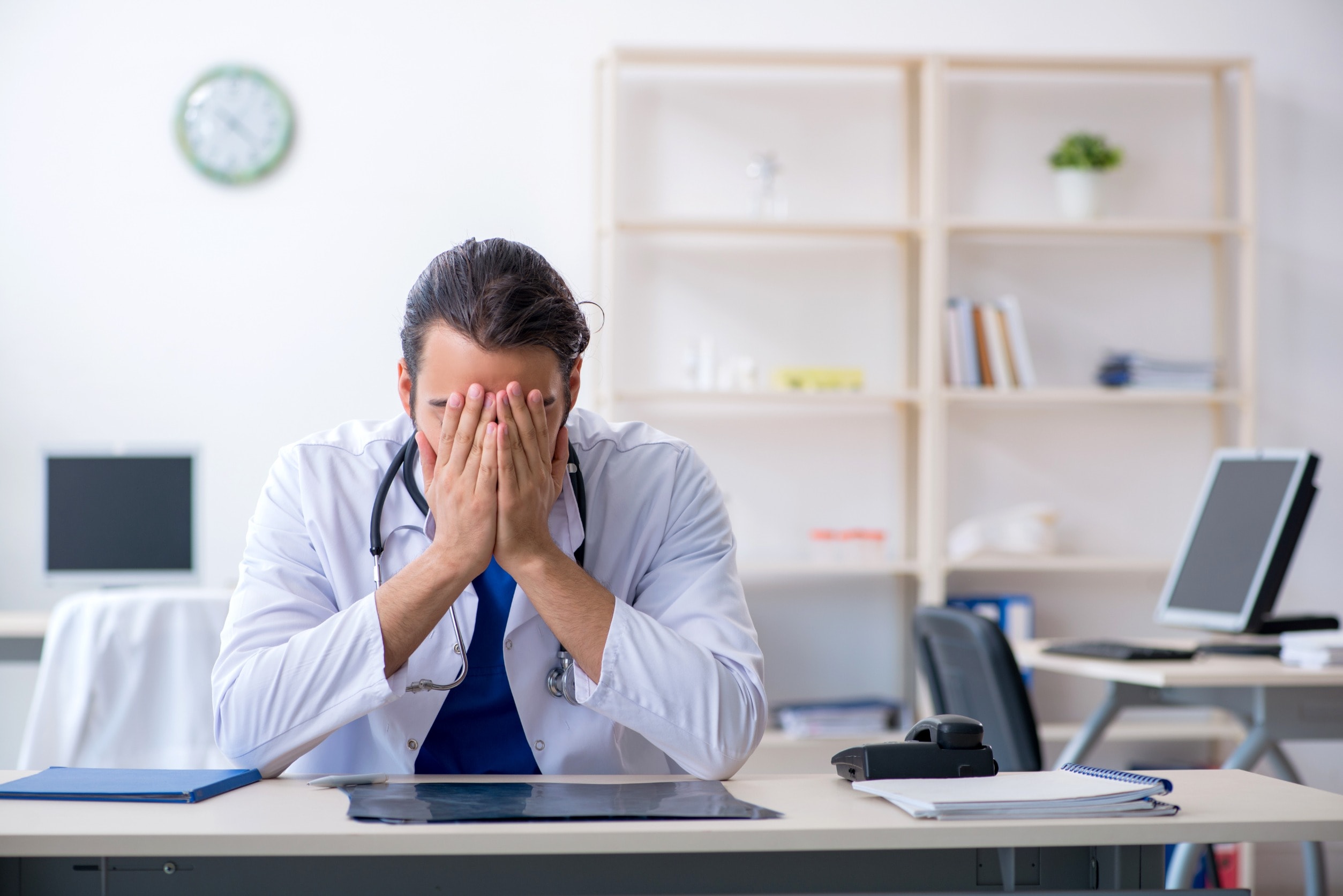 A doctor sits at his desk with his head in his hands after giving a patient negligent treatment