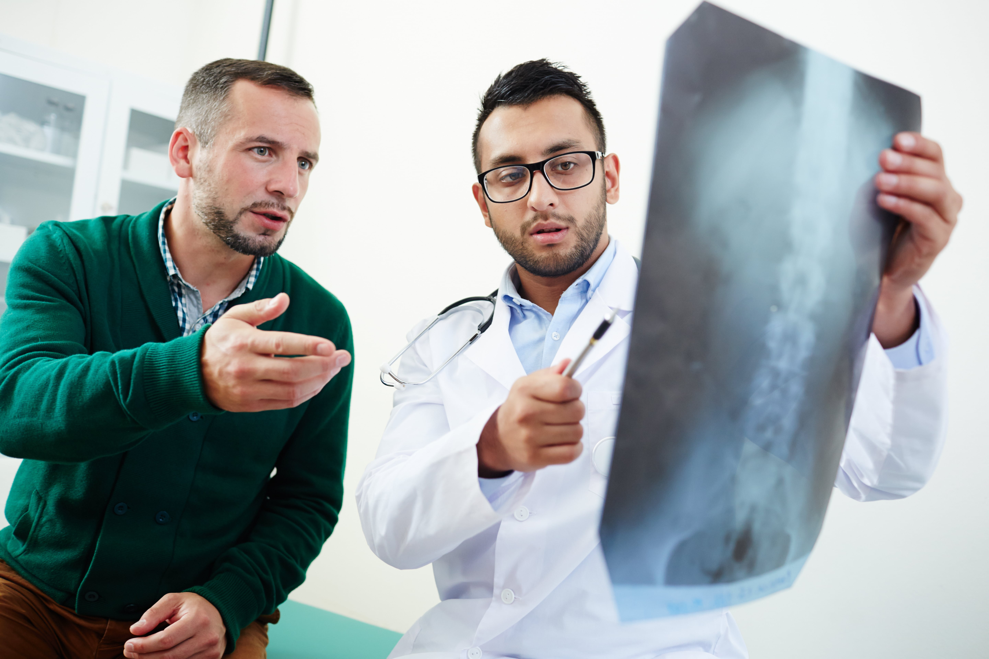 Man discussing results of imaging with a pain specialist. Doctor is holding up an MRI image.