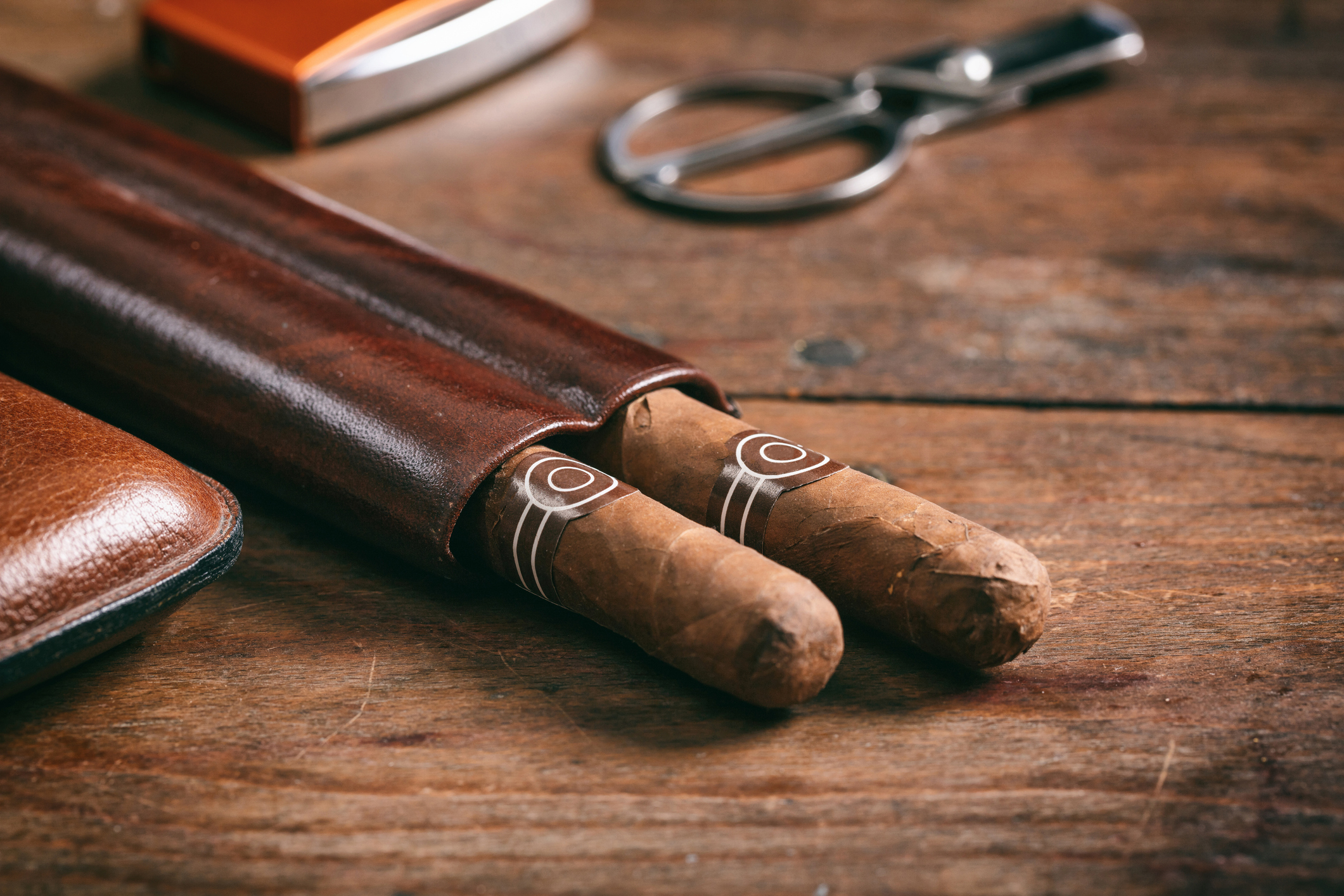 A leather cigar case with two cigars and cigar accessories