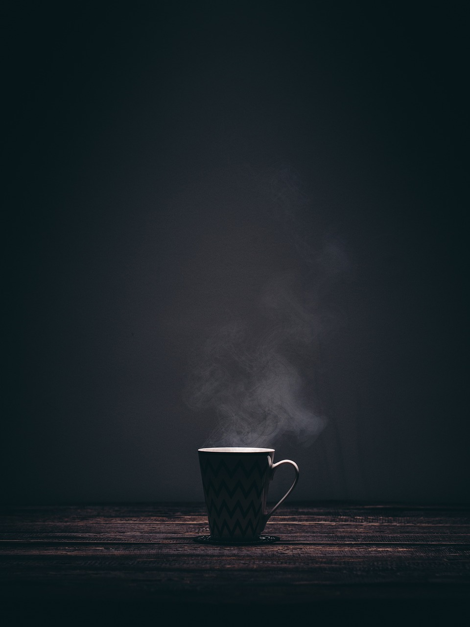 An image of a steaming cup of tea on a dark background.