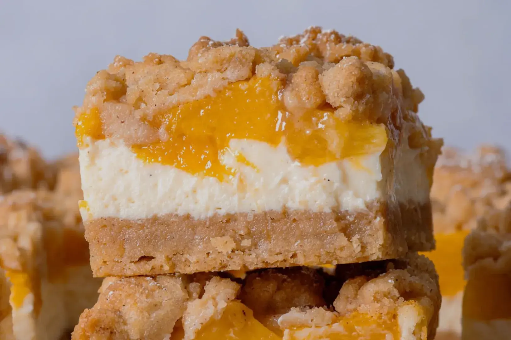 A close-up of a layered dessert bar featuring a crumbly topping, a creamy white layer, and a vibrant yellow fruit layer.