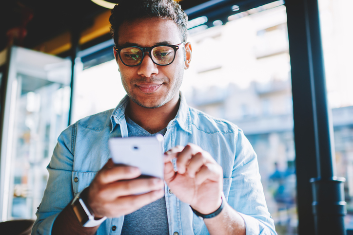 Dark-haired man in a blue shirt reading his email on his cell phone. 