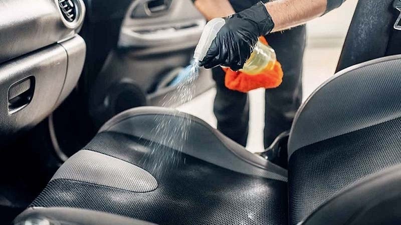 A man is spraying cleaning solution on the car seat