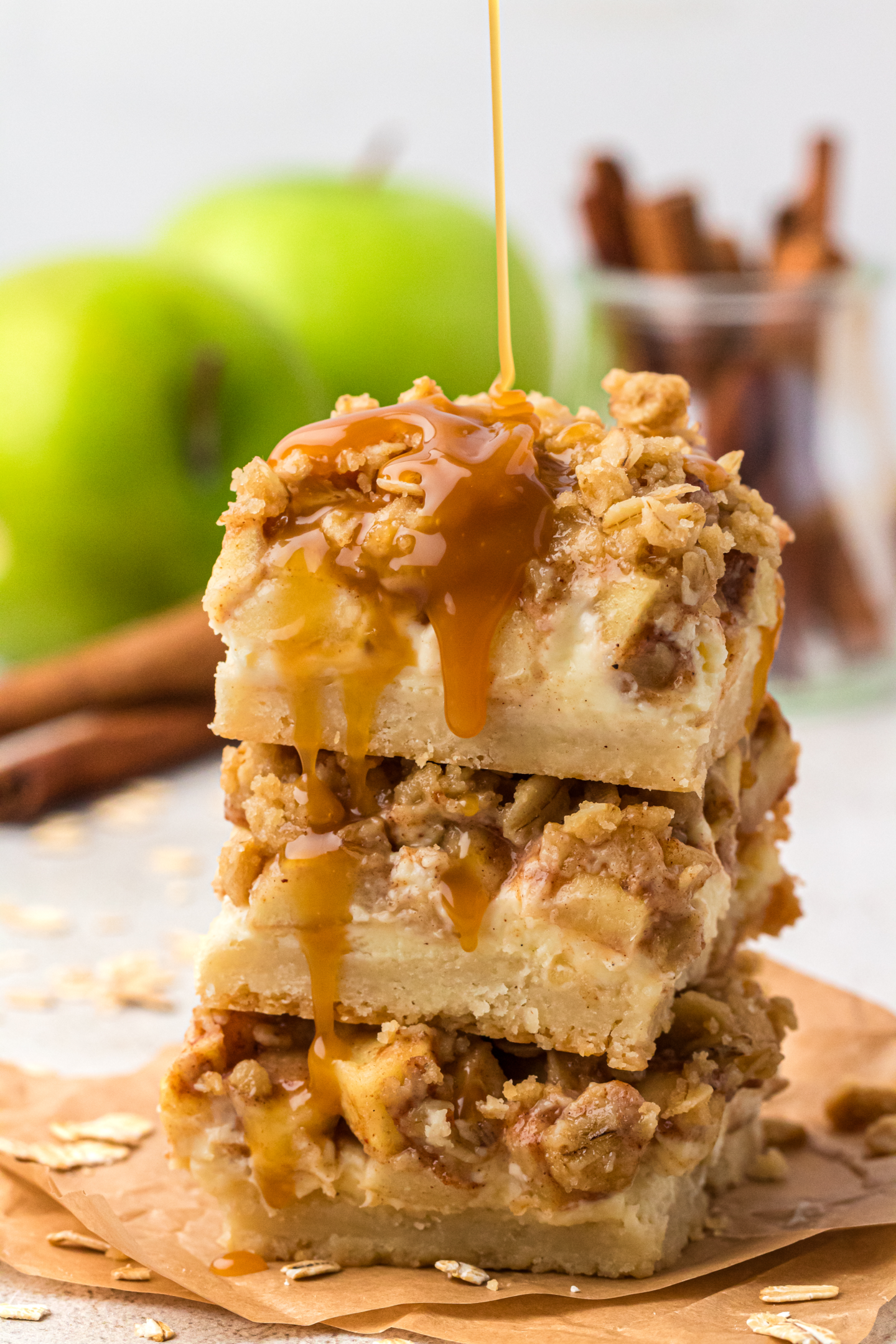 three caramel apple cheesecake bars stacked on top of each drizzled with caramel sauce