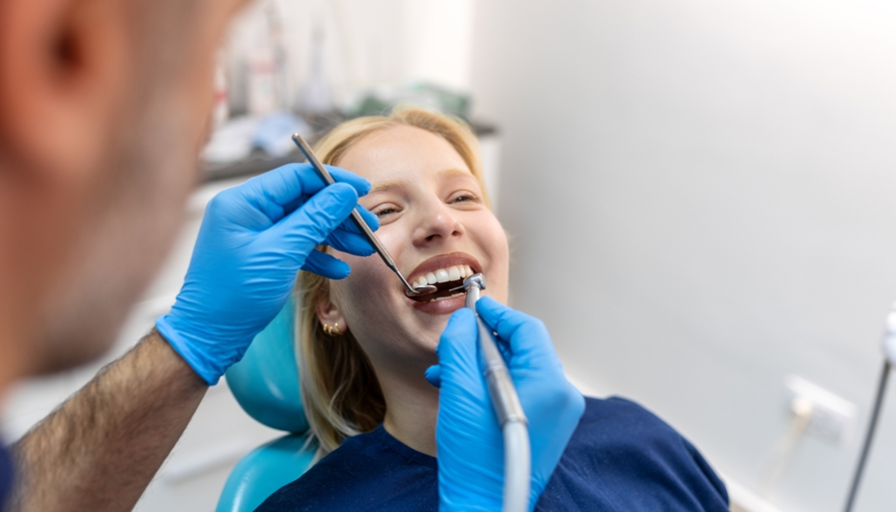 Mistet fylling i tann: Hva du må gjøre umiddelbart 9 Kvinne sitter i tannlegestol mens tannlegen undersøker og rengjør tennene hennes med blå hansker og instrumenter.