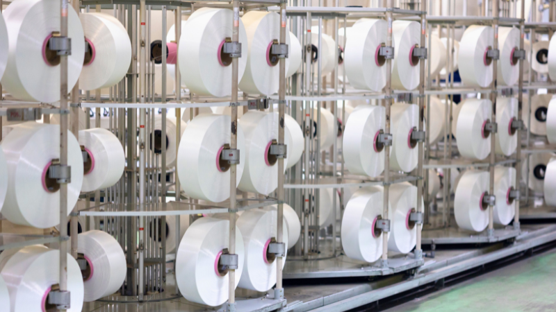 A large industrial setup with rows of large white spools of thread or yarn on metal racks.