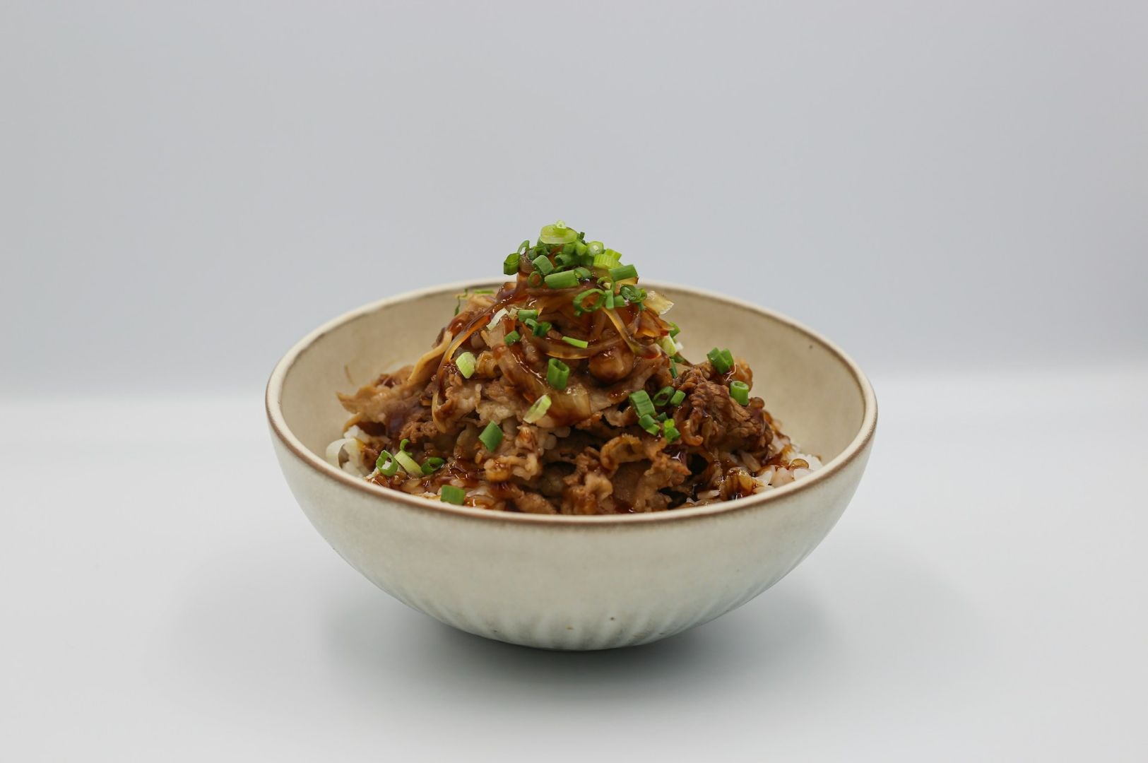 A bowl of savory beef with green onions and brown sauce, served over white rice. The dish exudes a warm, comforting and appetizing appeal.
