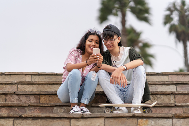 Two friends sitting on steps looking at a cell phone. 