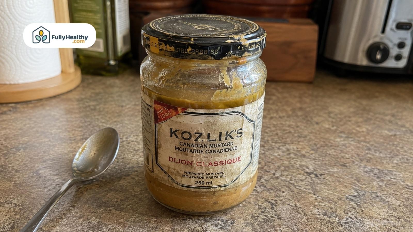 Open mustard jar on kitchen counter with spoon showing leftover condiment