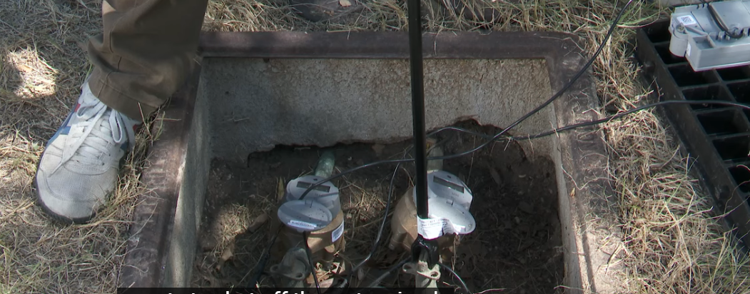 The image shows a residential water shutoff valve located near a water meter, which is essential for preventing water damage in case of burst pipes or flooding. Properly using this valve can help mitigate health risks associated with standing water and mold growth during flood cleanup efforts.