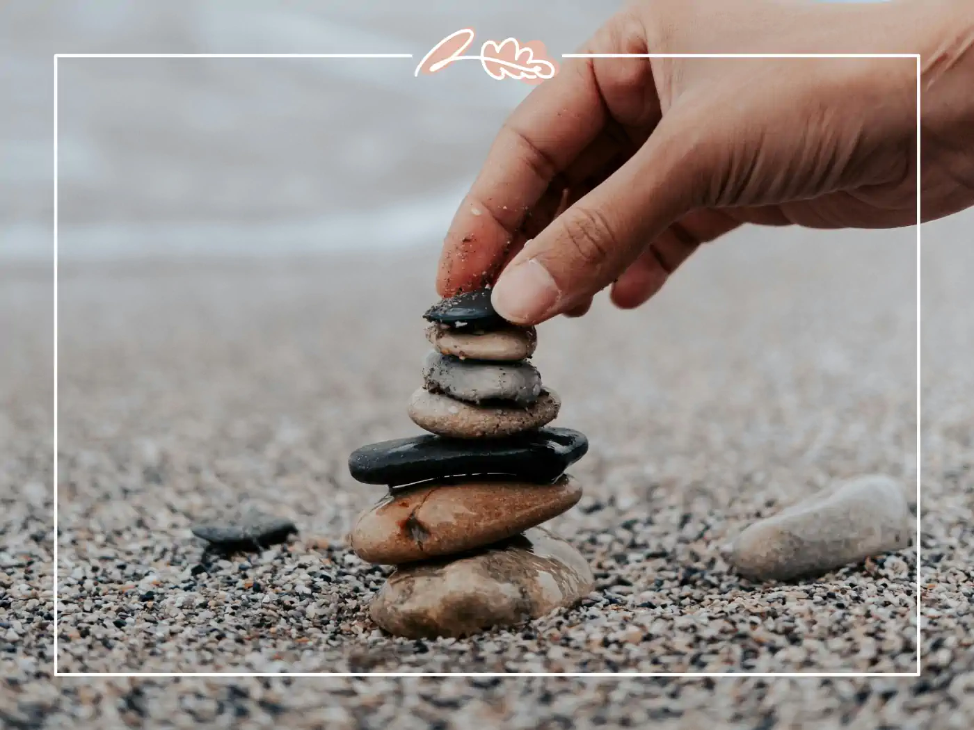 A hand stacking smooth stones on a pebble beach, representing balance and mental clarity in daily life.