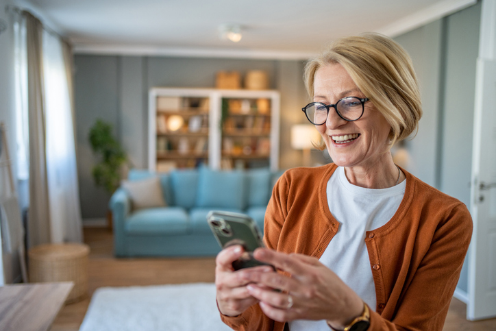 Short-haired blonde woman in glasses sending a text in her living room. 