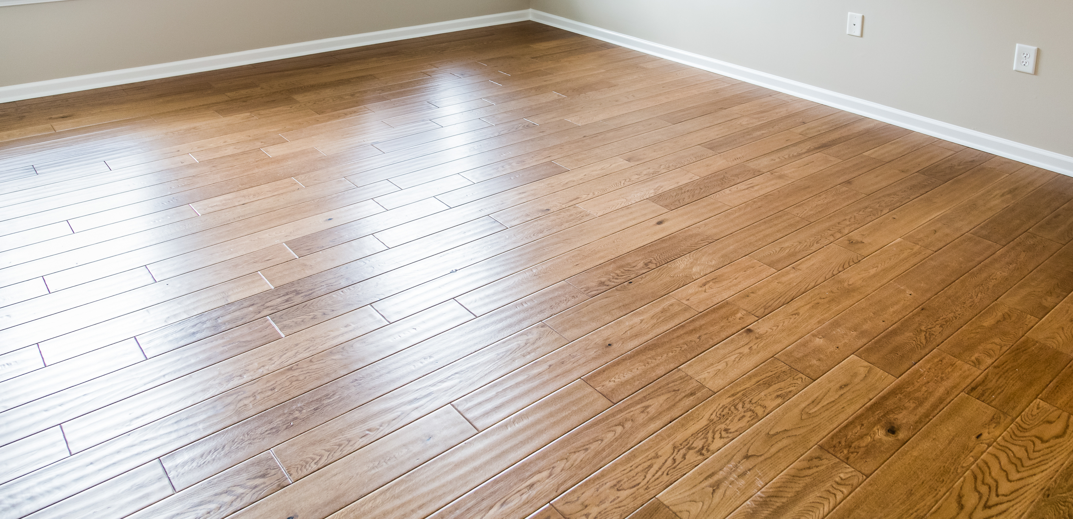 An empty room with a laminate floor. The floor has a pattern of interlocking planks with varying shades of brown and visible wood grain textures. 