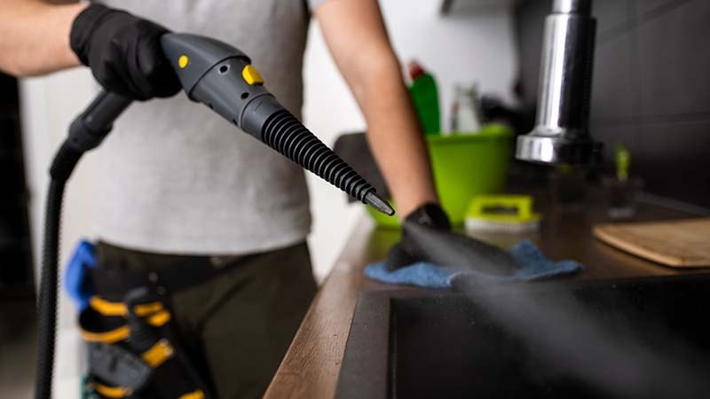 A man is using a steam cleaner on a car carpet