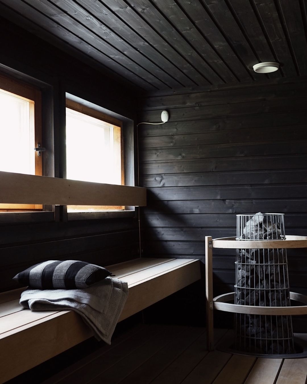 Moderni tumman sävyinen sauna ja vaaleat lauteet.