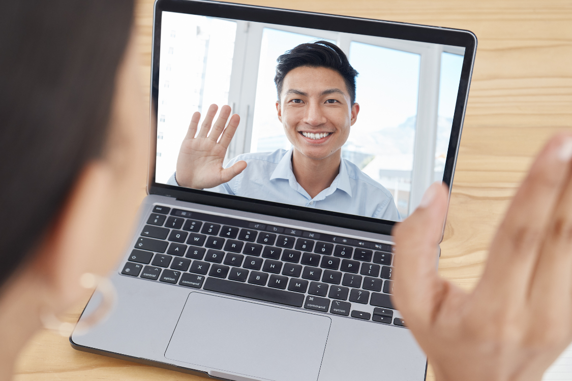 Close-up of a virtual one-on-one meeting with a smiling Filipino remote employee waving on video call