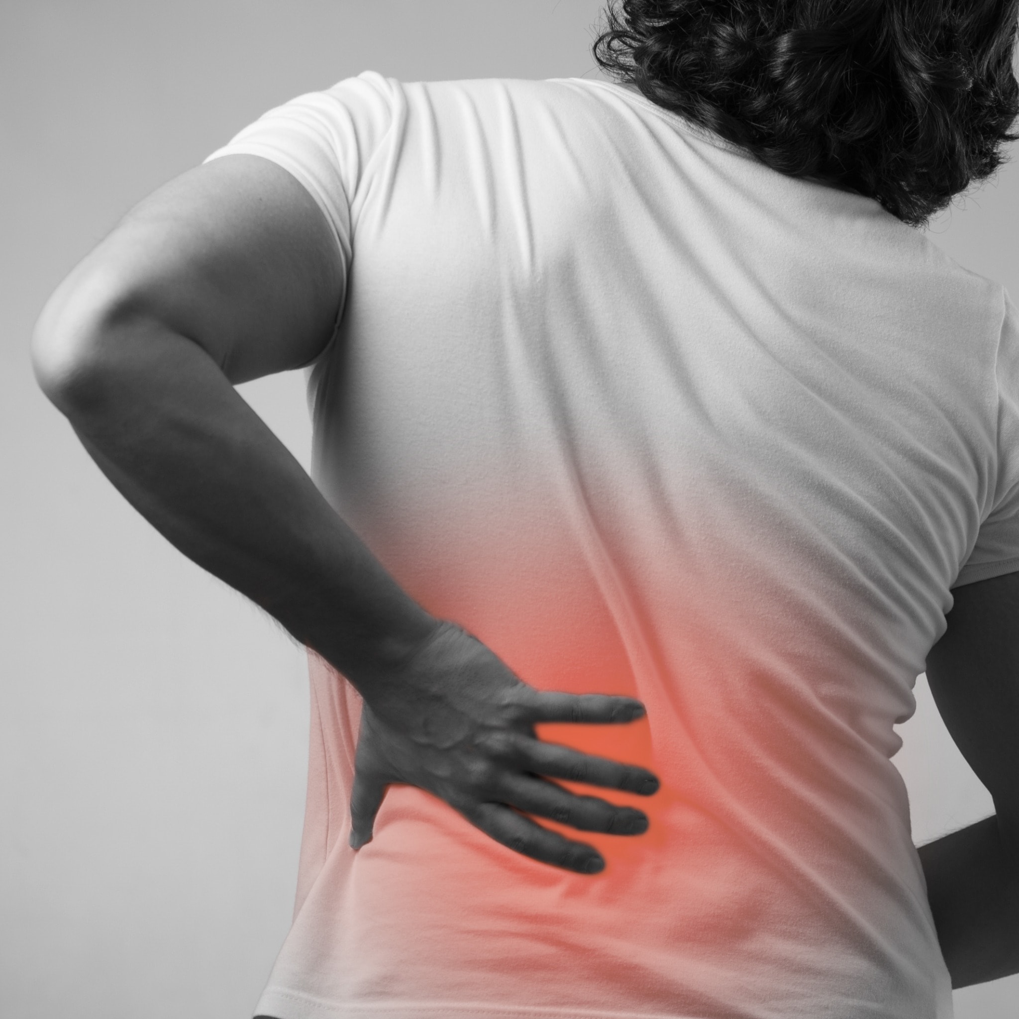 A man in a white tshirt holds his back in pain